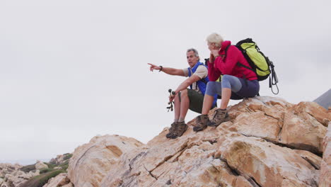Senior-hiker-couple-with-backpack-and-trekking-poles-pointing-towards-a-direction-and-talking