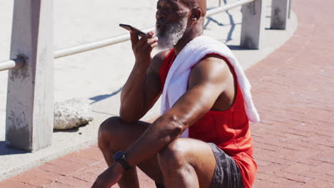 Senior-african-american-man-talking-on-the-smartphone-while-sitting-on-basketball-on-the-court-near-