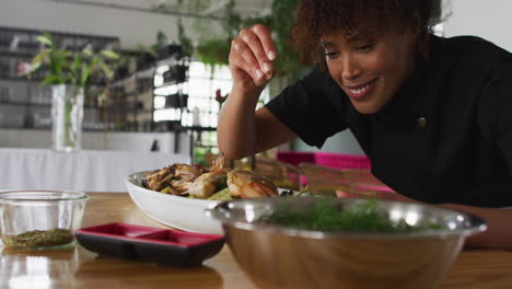 Mixed-race-female-chef-preparing-a-dish-and-smiling-in-a-kitchen-