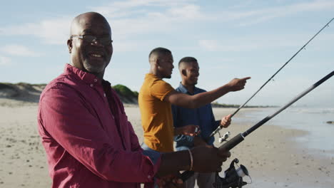 Afroamerikanischer-älterer-Vater-Und-Zwei-Söhne-Im-Teenageralter,-Die-Am-Strand-Stehen-Und-Angeln-Und-Reden