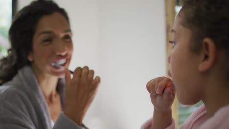 Happy-mixed-race-mother-and-daughter-brushing-teeth-in-bathroom
