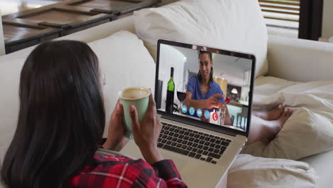 Afroamerikanische-Frau-Hält-Eine-Kaffeetasse-In-Der-Hand-Und-Führt-Einen-Videoanruf-Auf-Dem-Laptop,-Der-Zu-Hause-Auf-Der-Couch-Sitzt