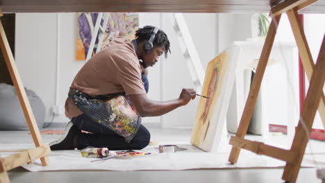 Artista-Masculino-Afroamericano-Con-Auriculares-Pintando-Sobre-Lienzo-En-El-Estudio-De-Arte
