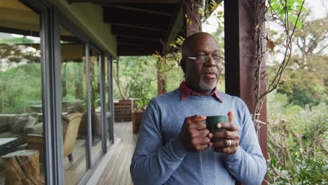 Afroamerikanischer-älterer-Mann,-Der-Auf-Dem-Balkon-Steht,-Kaffee-Trinkt-Und-Die-Aussicht-Genießt