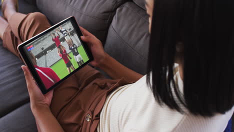 Composite-of-woman-sitting-at-home-on-couch-watching-rugby-match-on-tablet