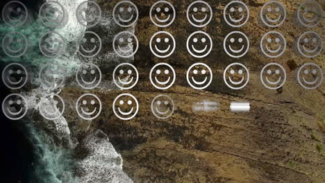 Digital-composition-of-rows-of-multiple-smiling-face-emojis-against-aerial-view-of-sea-waves