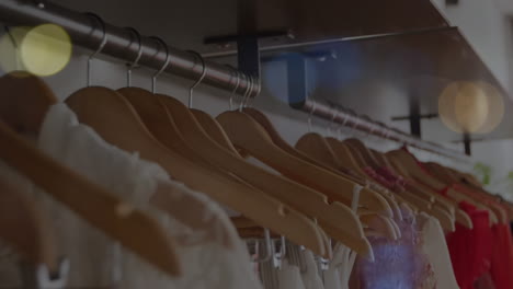Animation-of-bokeh-lights-over-clothes-hanging-on-display-in-shop