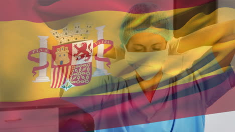 Spanish-flag-waving-against-caucasian-female-health-worker-wearing-face-mask-at-hospital