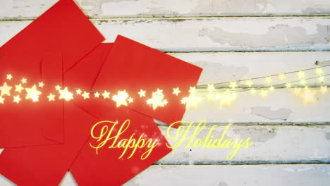 Animation-of-text,-happy-holidays,-in-yellow,-over-string-lights-and-red-envelopes-on-white-boards