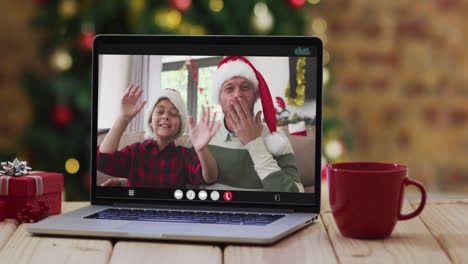 Glücklicher-Vater-Und-Sohn-Winken-Bei-Einem-Videoanruf-Auf-Dem-Laptop,-Mit-Weihnachtsdekorationen-Und-Baum