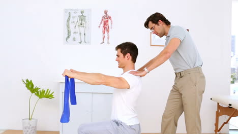 Physiotherapeut-überprüft-Die-Schultern-Des-Patienten,-Der-An-Einem-Widerstandsband-Zieht