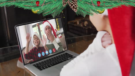 Animation-of-christmas-decorations-over-caucasian-girl-in-santa-hat-on-laptop-video-call-with-family