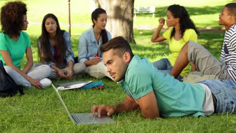 Smiling-student-using-his-laptop-in-front-of-his-friends