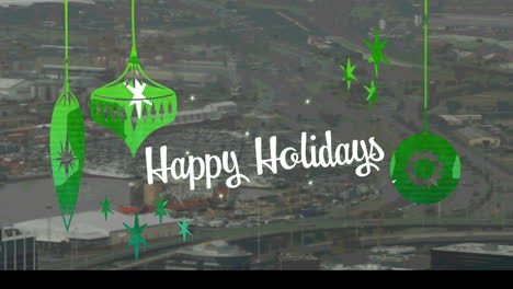 Happy-holidays-text-with-green-christmas-hanging-decorations-against-aerial-view-of-cityscape