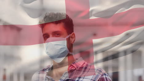Animation-of-flag-of-england-waving-over-man-wearing-face-mask-during-covid-19-pandemic