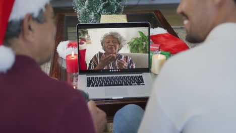 Lächelnder,-Gemischtrassiger-Vater-Und-Sohn,-Die-Einen-Laptop-Für-Einen-Weihnachtsvideoanruf-Mit-Einer-älteren-Frau-Auf-Dem-Bildschirm-Nutzen