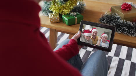 Caucasian-man-using-tablet-and-waving-for-christmas-video-call-with-smiling-family-on-screen