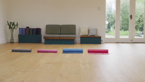 Four-rolled-up-yoga-mats-in-empty-studio-with-wooden-floor-and-doors-to-garden