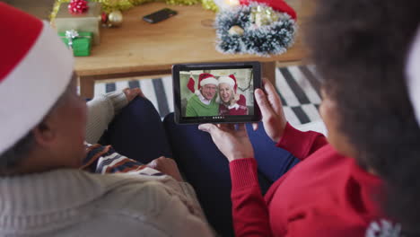 African-american-mother-and-daughter-using-tablet-for-christmas-video-call-with-couple-on-screen