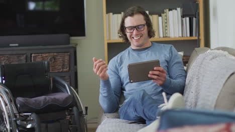 Happy-caucasian-disabled-man-sitting-on-sofa-in-living-room-using-tablet
