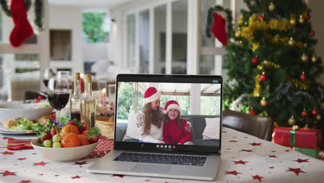Happy-caucasian-mother-and-daughter-in-santa-hats-on-laptop-lying-on-christmas-table