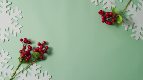 Video-of-christmas-leaf-and-red-berry-decorations-with-snowflake-patterns-and-copy-space-on-green