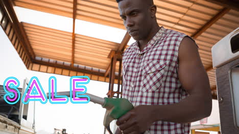 Animation-Des-Verkaufstextes-In-Neon-über-Einem-Afroamerikanischen-Mann,-Der-Die-Kraftstoffpumpe-An-Der-Tankstelle-Benutzt