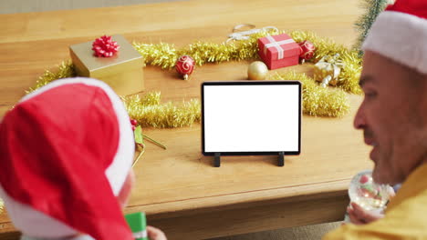 Caucasian-father-with-son-in-santa-hats-making-tablet-christmas-video-call,-copy-space-on-screen