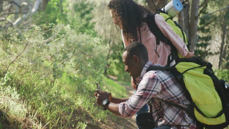 Smiling-diverse-couple-taking-photo-with-smartphone-and-hiking-in-countryside
