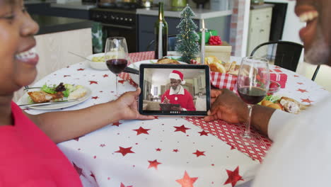 Afroamerikanisches-Paar-Mit-Wein-Und-Tablet-Für-Einen-Weihnachtsvideoanruf-Mit-Dem-Weihnachtsmann-Auf-Dem-Bildschirm