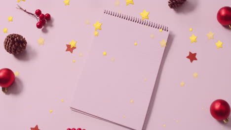Animation-of-gold-stars-falling-over-christmas-decorations-and-notepad-with-copy-space