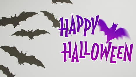 Fröhliches-Halloween-Textbanner-Mit-Fledermaussymbol-Vor-Mehreren-Fledermausspielzeugen-Auf-Grauer-Oberfläche