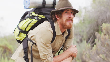 Portrait-of-happy-bearded-caucasian-male-survivalist-with-backpack,-enjoying-wilderness-scenery