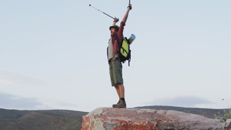 Happy-caucasian-male-survivalist-celebrating-with-arms-in-the-air-on-mountain-peak-in-wilderness
