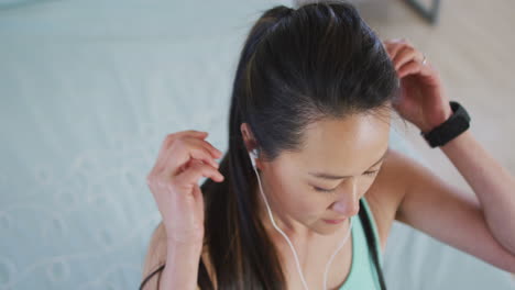 Porträt-Einer-Asiatischen-Frau,-Die-Kopfhörer-Trägt,-Sich-Auf-Das-Training-Vorbereitet-Und-Haare-Bindet