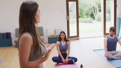 Caucasian-female-instructor-explaining-to-diverse-man-and-woman-sitting-on-mats-at-yoga-class