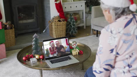Senior-caucasian-woman-waving-and-using-laptop-for-christmas-video-call-with-couple-on-screen