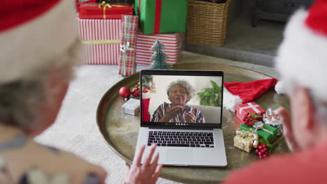 Senior-caucasian-couple-with-santa-hats-using-laptop-for-christmas-video-call-with-woman-on-screen