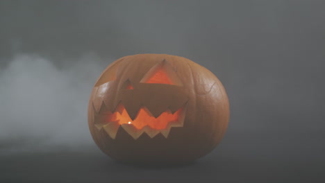 Raucheffekt-über-Gruseligem-Gesicht-Geschnitzter-Halloween-Kürbis-Vor-Grauem-Hintergrund