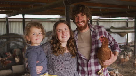 Portrait-of-smiling-caucasian-family-holding-chicken,-looking-at-camera