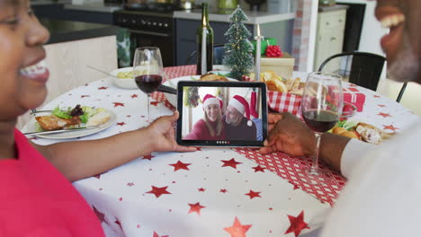 Smiling-african-american-couple-using-tablet-for-christmas-video-call-with-couple-on-screen