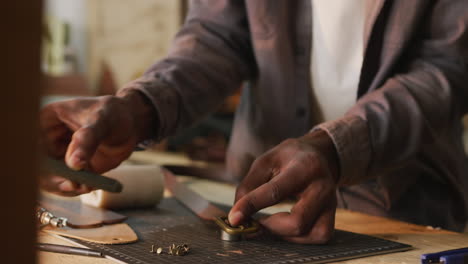 Hands-of-african-american-craftsman-using-tools-to-make-a-belt-in-leather-workshop