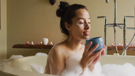 Entspannte-Gemischtrassige-Frau,-Die-Mit-Schaum-In-Der-Badewanne-Liegt-Und-Kaffee-Trinkt