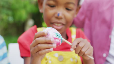 Animation-of-happy-african-american-girl-painting-easter-eggs-in-garden