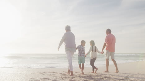 Happy-hispanic-grandparents-and-grandchildren-walking-on-beach-at-sunset