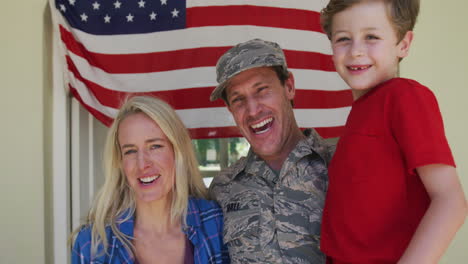 Portrait-of-caucasian-male-soldier-embracing-his-wife-and-son-over-american-flag