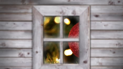 Animation-of-snow-falling-over-christmas-tree-and-red-bauble-seen-through-window