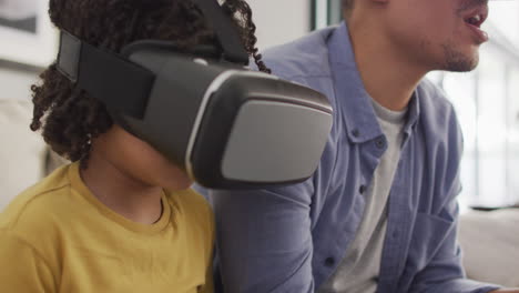 Happy-biracial-man-and-his-son-playing-video-games-wearing-vr-headset