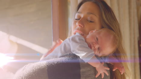 Animation-of-glowing-spots-over-happy-caucasian-mother-with-sleeping-baby