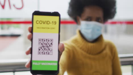 African-american-businesswoman-with-face-mask-preparing-covid-19-certification-on-smartphone